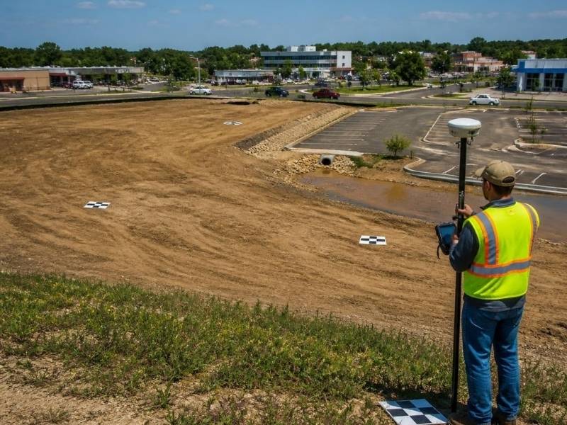 Surveyor measuring ground control points for a commercial drone mapping project in St. Petersburg, FL while a survey drone collects aerial data.